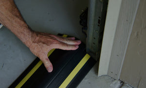 Une main appliquant une barrière anti-inondation de porte de garage au sol du garage